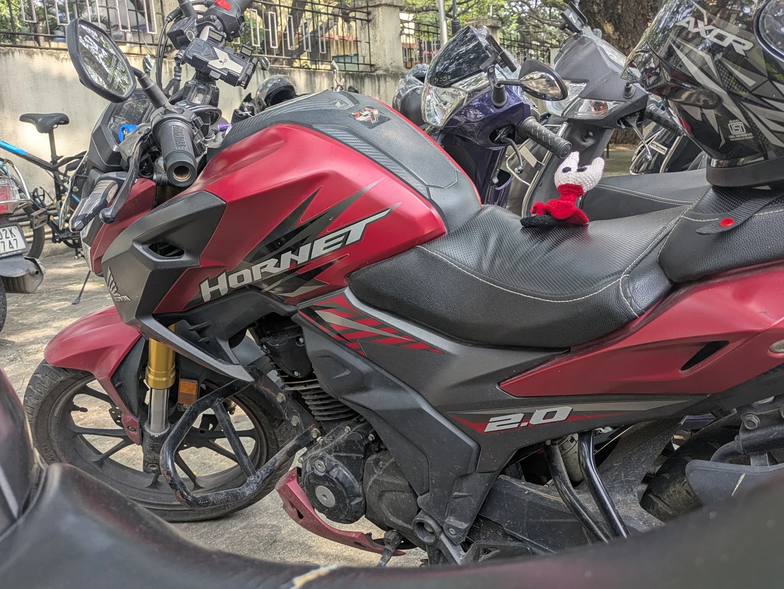 A red Honda Hornet parked on the street, with a small crocheted toy on the seat.
